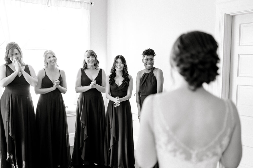 Bridesmaids react with joy and excitement as they see the bride for the first time in her wedding dress, capturing a candid and emotional moment before the ceremony in Napa Valley, CA.