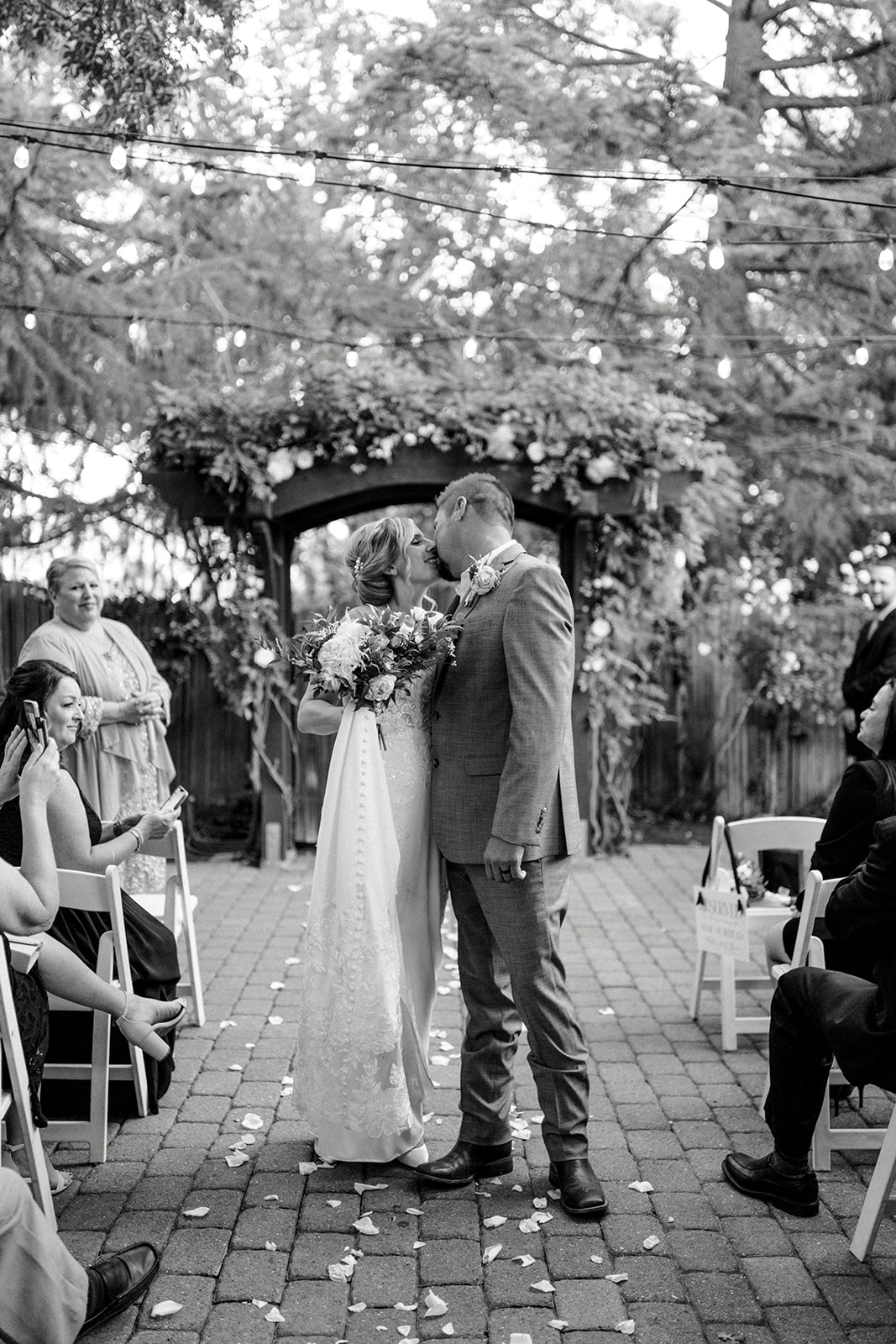 Bride and groom share a romantic kiss as they walk down the aisle after their ceremony, captured in a timeless black-and-white photo at Wine and Roses.