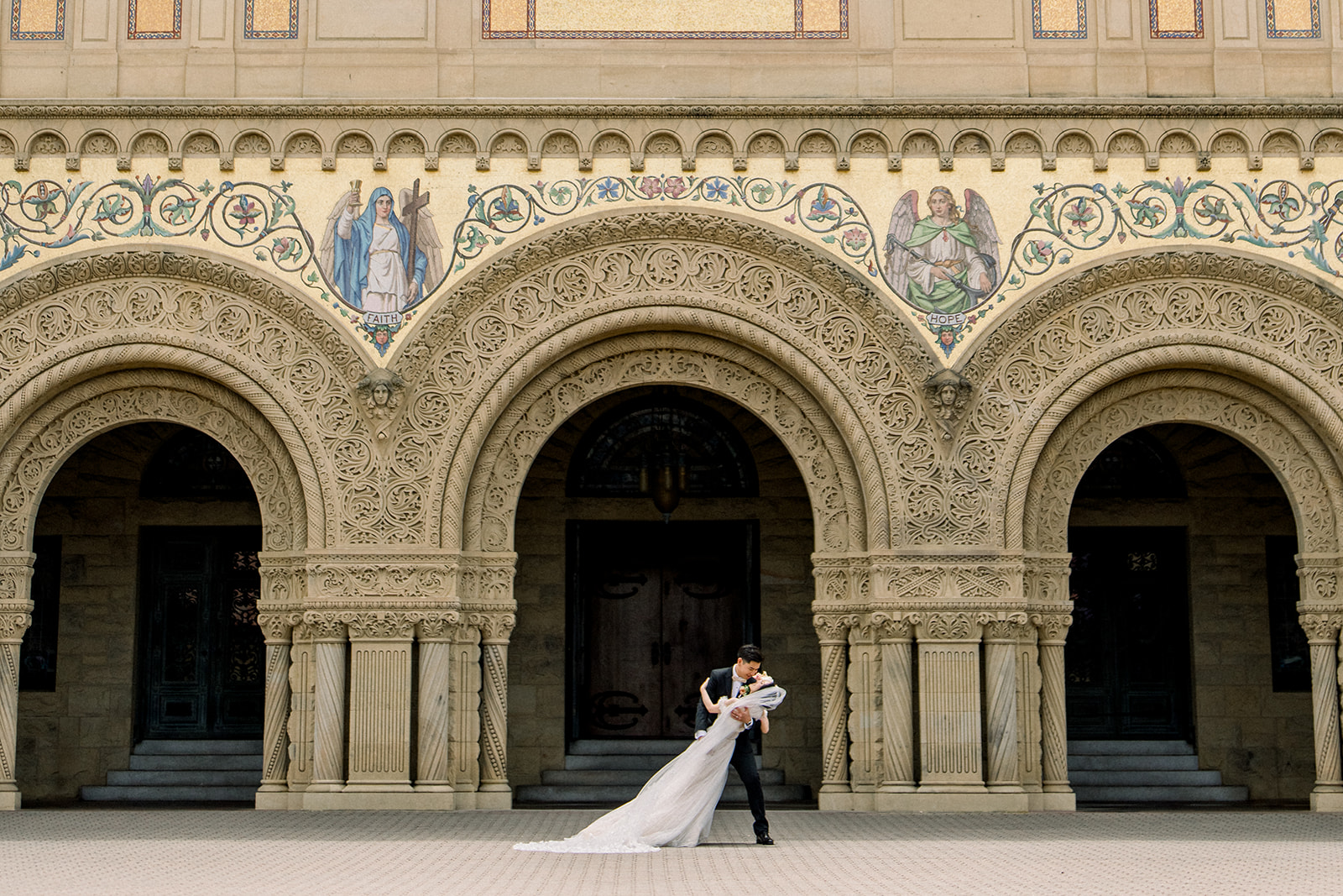 Bride and groom sharing a romantic dip in front of the ornate arches of Stanford Memorial Church, showcasing the elegance and grandeur of their wedding day.