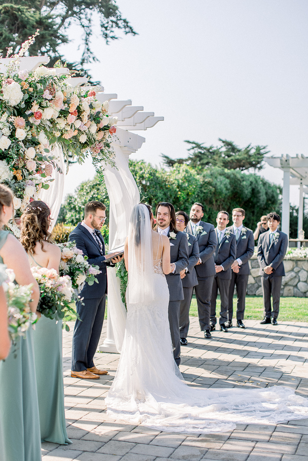 Bride and groom exchange vows under a floral-adorned pergola at their Half Moon Bay wedding.