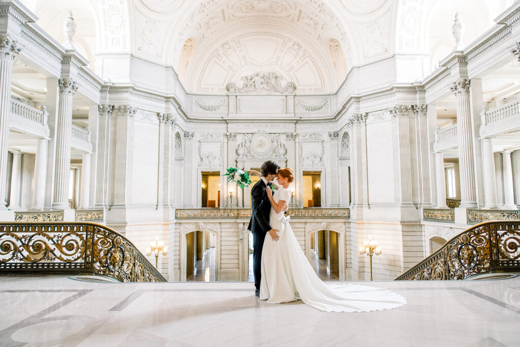 Couple sharing a romantic moment on the grand staircase inside San Francisco City Hall, a classic venue for their San Francisco wedding.