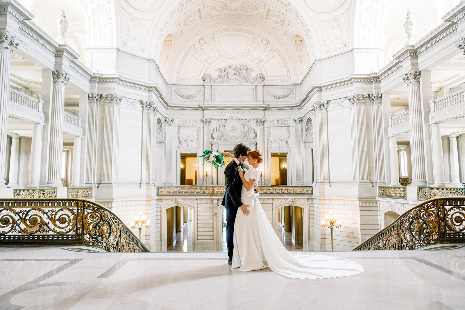 Couple sharing a romantic moment on the grand staircase inside San Francisco City Hall, a classic venue for their San Francisco wedding.