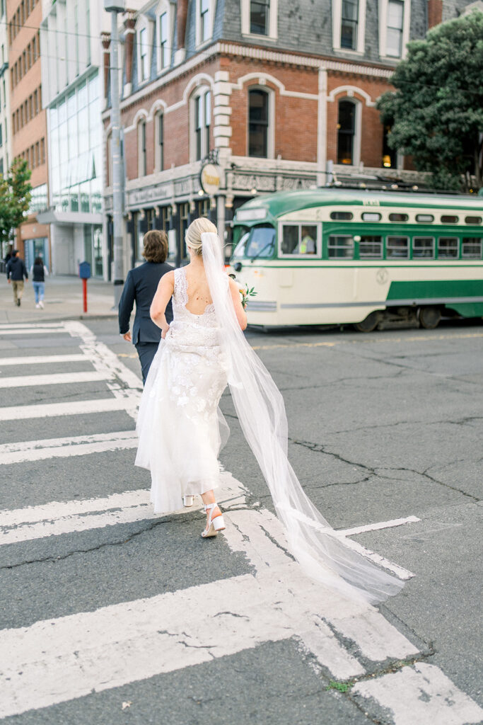 Bride and Groom walking across a San Francisco street with a classic streetcar in the background, capturing the urban charm of a San Francisco wedding.