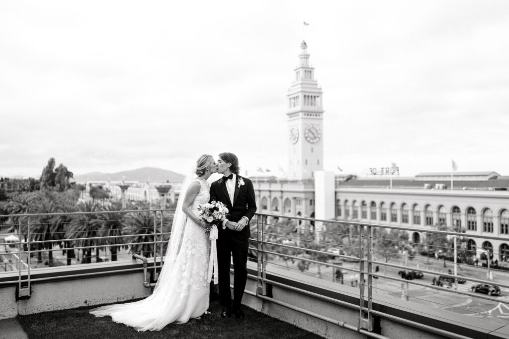 Bride and groom sharing a kiss on a rooftop with the San Francisco Ferry Building in the background during their San Francisco wedding.