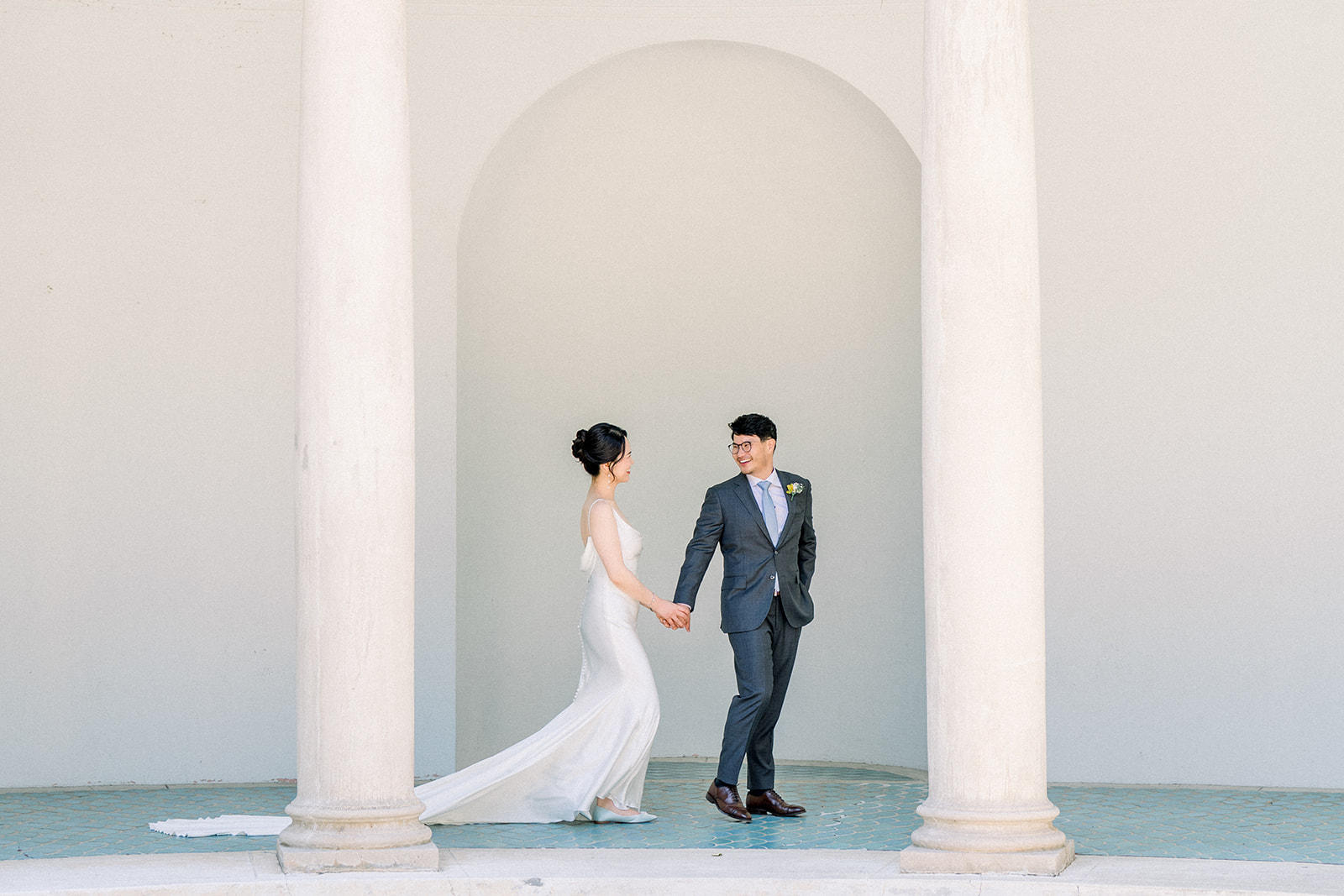 Bride and groom holding hands as they walk between stone columns at the Pavilion at Hacienda de las Flores in Moraga