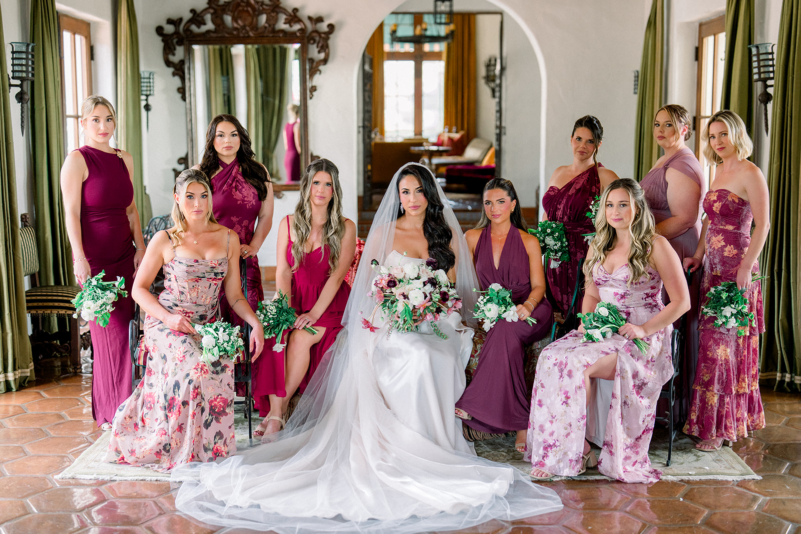 Bride and bridesmaids in rich berry and floral-toned dresses gathered inside Hummingbird Nest Ranch, styled for a luxury California wedding.