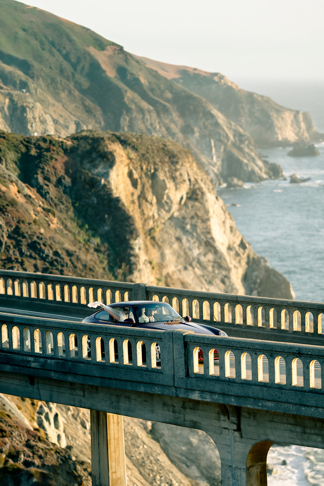 Vintage Porsche crossing Bixby Bridge with the Big Sur coastline stretching beyond on a honeymoon session