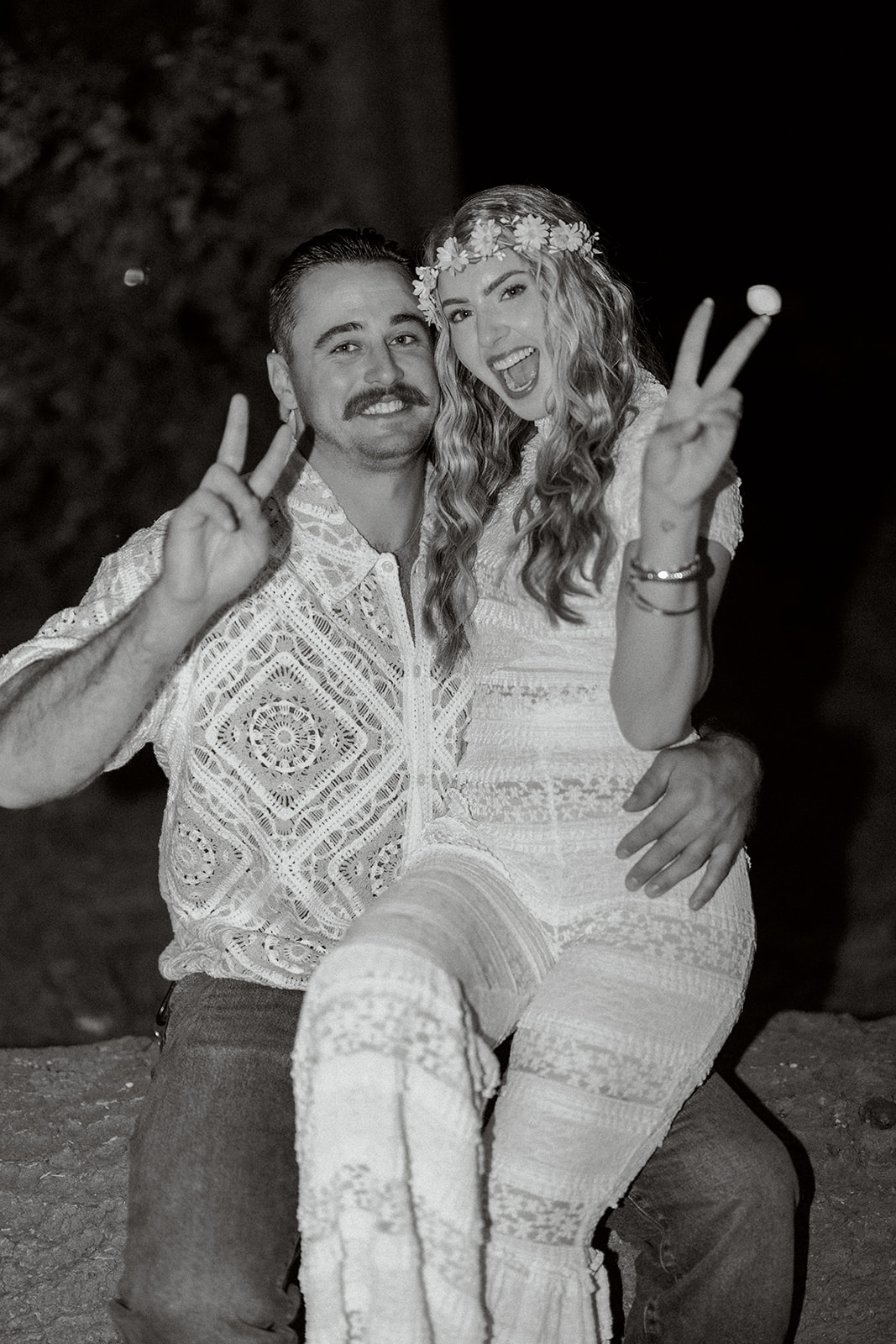 Black and white photo of a couple making peace signs at their Summer of Love wedding welcome party at Evergreen Lodge